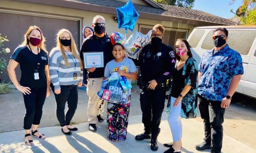 Child winning a scholarship. Friends and officers are around them with balloons and a certificate.